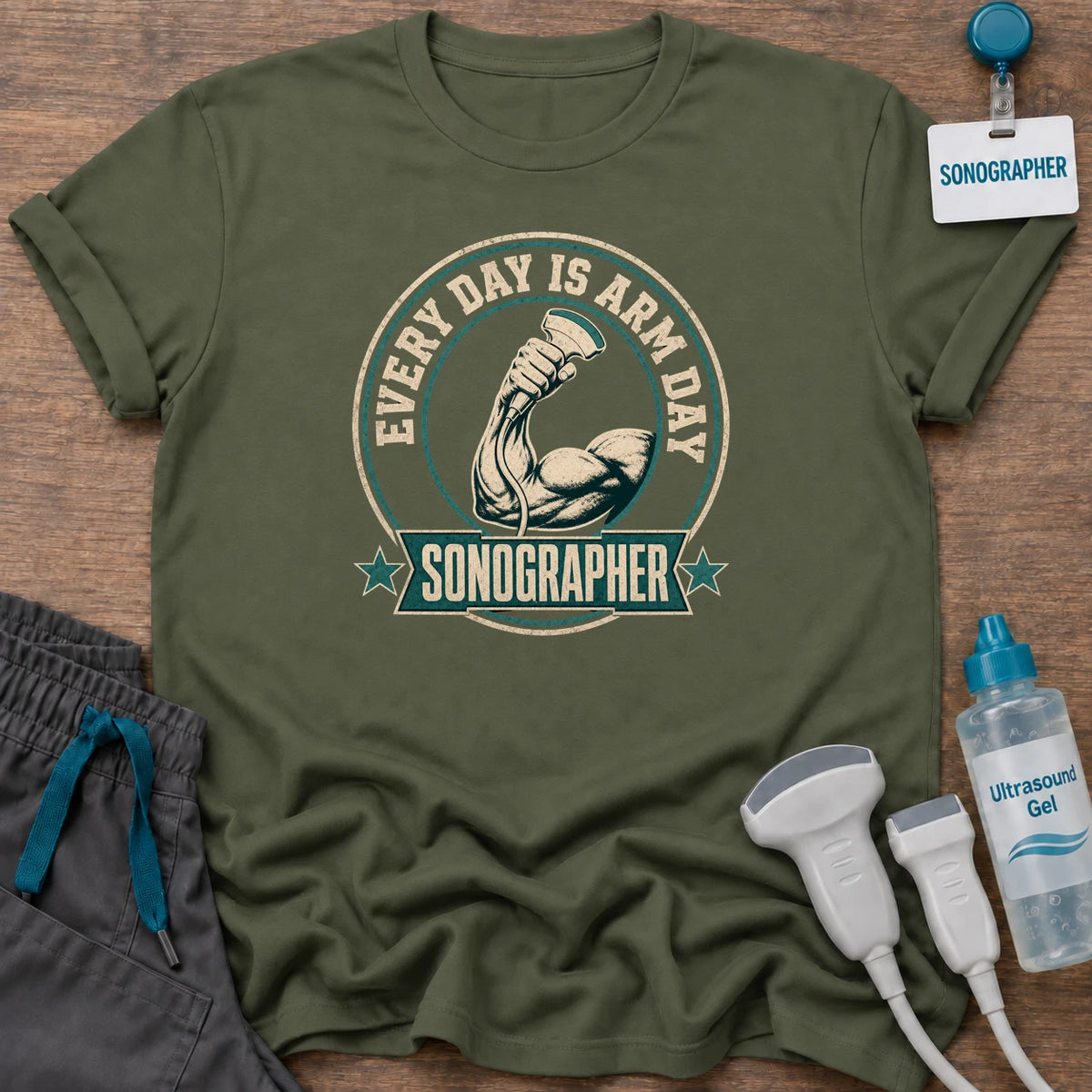 Arm Day Sonographer Badge t-shirt with a vintage circular badge with a muscular arm holding an ultrasound probe, “Every Day Is Arm Day” and a “Sonographer” banner with stars, in Military Green, by Sono Graphics