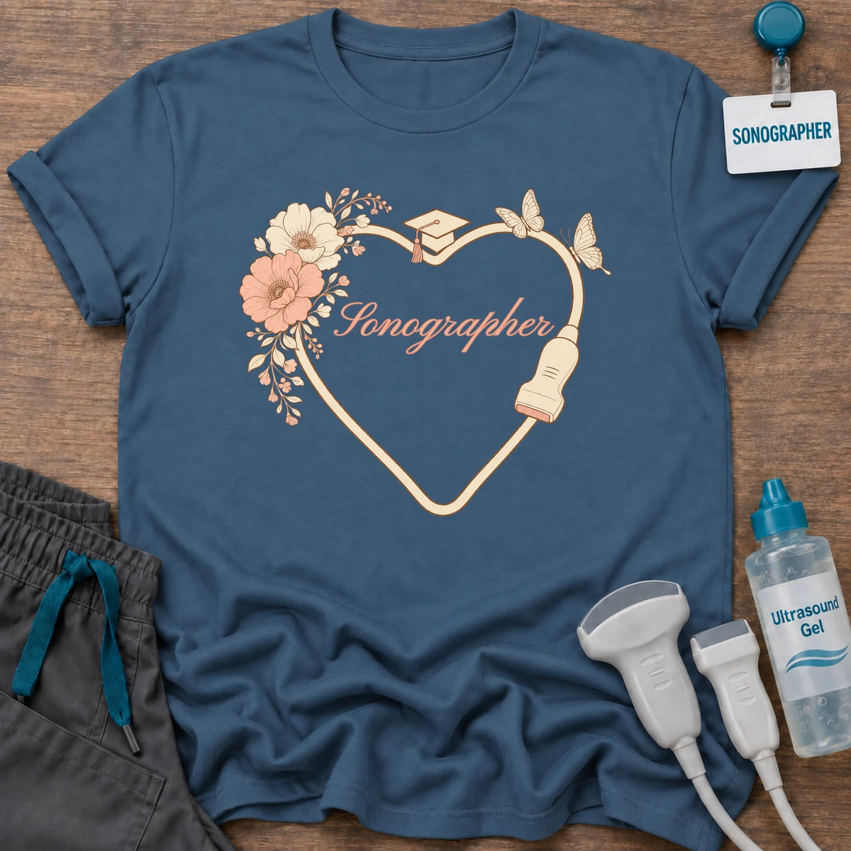 Sonography Graduate Floral Heart t-shirt with a heart drawn by a transducer cord with blush flowers, a graduation cap, butterflies and “Sonographer” in peach script, in Indigo Blue, by Sono Graphics